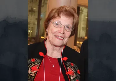 Helen Murray Free smiling at the camera, wearing a red shirt and black jacket with red trim.